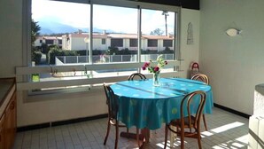 A dining area with a table and chairs, a window with a view of buildings, and a ceiling with wooden beams.