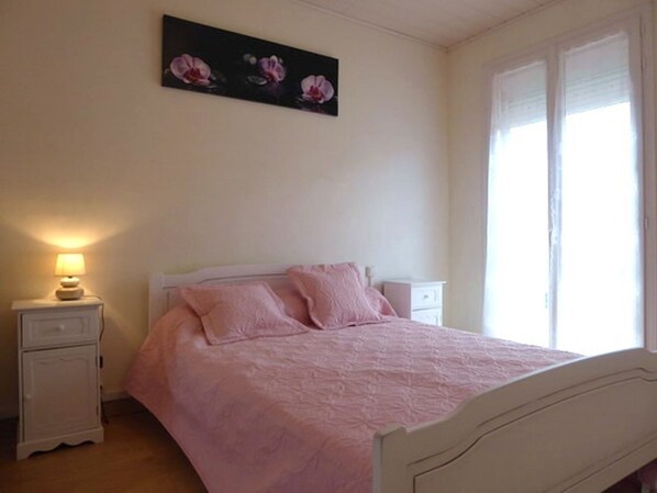A bedroom with a bed, a nightstand, a lamp, and a window with blinds.