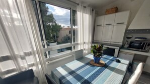 A small kitchen with white cabinets, a microwave, and a small refrigerator. There is a table with a blue and white checkered tablecloth and a potted plant on it. - Air-conditioned 2-room apartment 4/5 pers with pool (Argelès-sur-Mer)