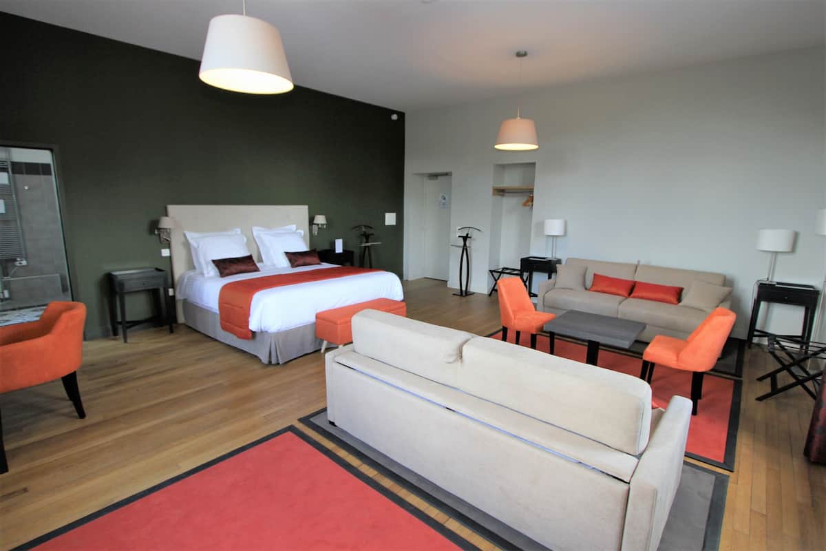 A hotel room with a bed, a sofa, two armchairs, a coffee table, and a desk.
