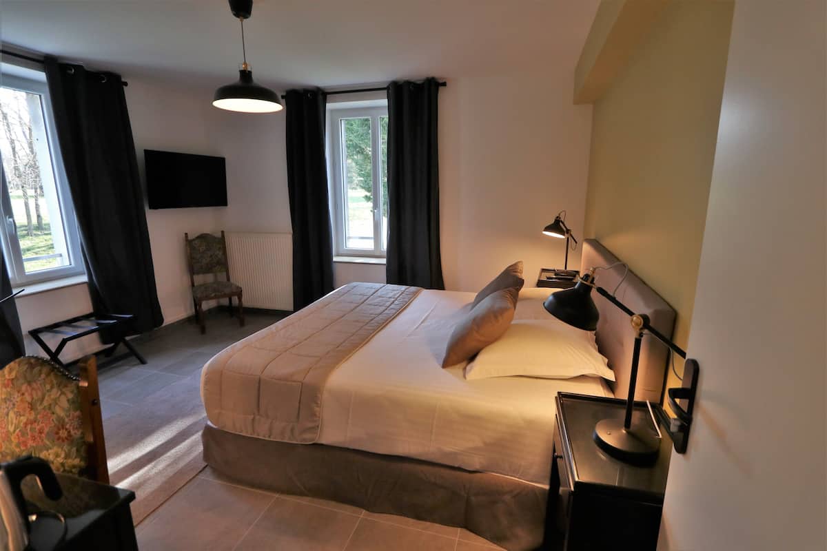 A bedroom with a bed, a chair, a desk, a lamp, and a TV on the wall.