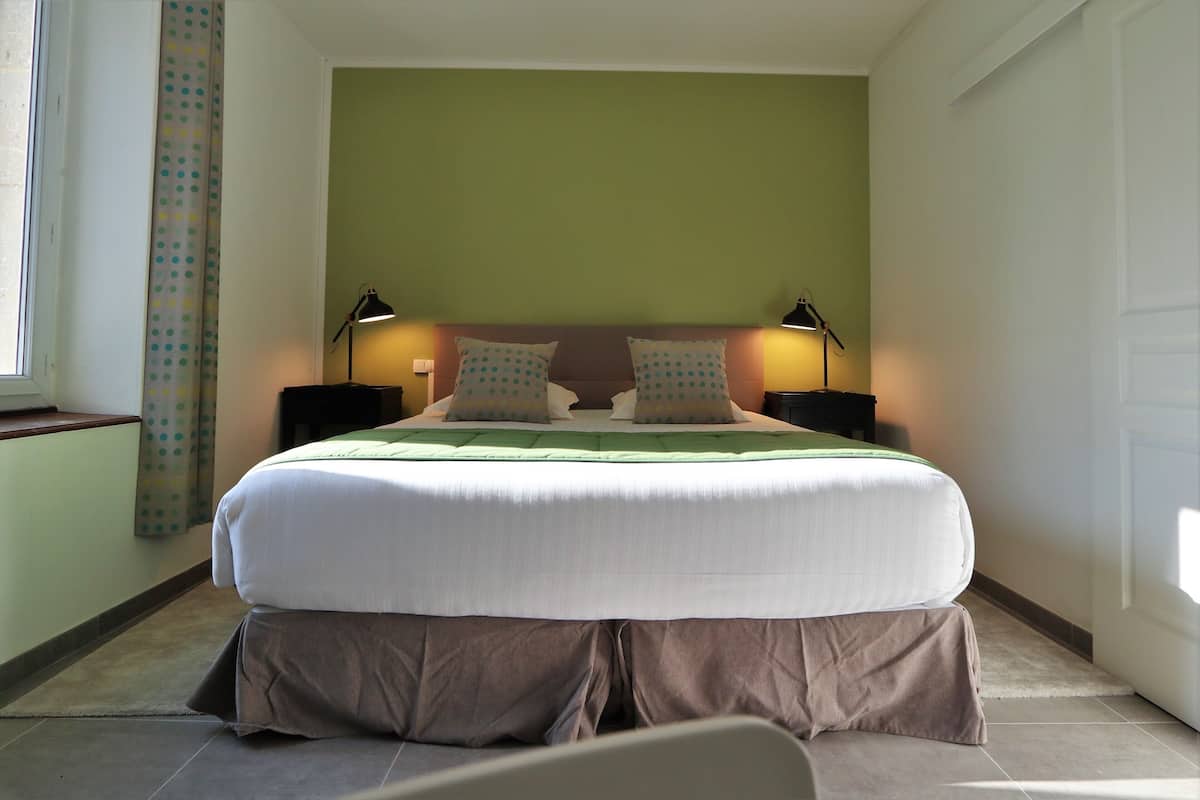 A neatly made bed with a green headboard, two bedside lamps, and a curtain with a polka dot pattern.