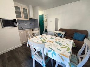 A compact kitchen with a microwave, stove, and cabinets, a dining table with chairs, and a sofa in a living area.