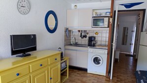 A compact kitchen with a washing machine, microwave, and a yellow cabinet with drawers. - Cozy Studio for 4 with Wi-Fi, Pool, Parking – 500m from Beach (Argelès-sur-Mer)