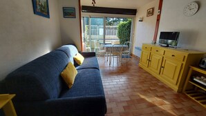 A living room with a blue sofa, yellow cushions, a yellow cabinet, and a television. - Cozy Studio for 4 with Wi-Fi, Pool, Parking – 500m from Beach (Argelès-sur-Mer)