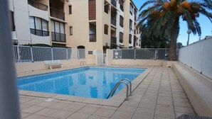 A swimming pool with a tiled deck, surrounded by a white fence and a palm tree. - Cozy Studio for 4 with Wi-Fi, Pool, Parking – 500m from Beach (Argelès-sur-Mer)