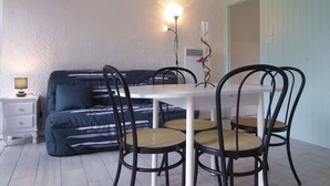 A small dining area with a white table and four chairs, a sofa, and a lamp.
