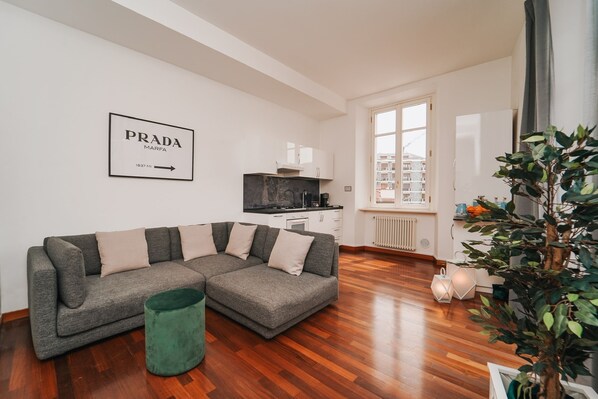 Una sala de estar moderna con un sofá seccional gris, un otomano verde y una planta grande en maceta.