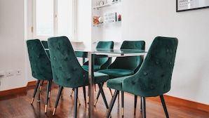 A dining area with a glass table surrounded by four green upholstered chairs with black and gold legs.