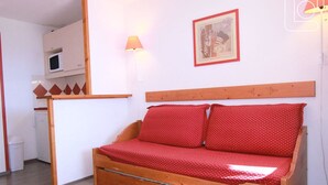 Une petite pièce agréable et chaleureuse, avec un lit en bois, un bureau équipé d’un ordinateur, une lampe et un tableau encadré accroché au mur.