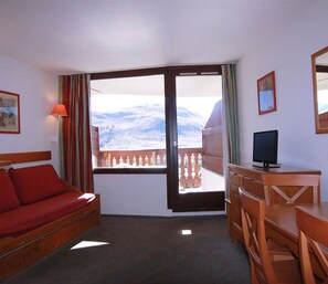 Ein Hotelzimmer mit Balkon, einem Bett, einem Schreibtisch und einem Fernseher.