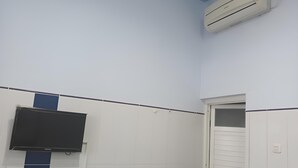 A room with a mounted TV, an air conditioning unit, and a door with a window. - Hotel Orchid Syariah (Tegal)