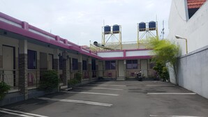 A parking area with a building in the background, including water tanks and a staircase. - Hotel Orchid Syariah (Tegal)
