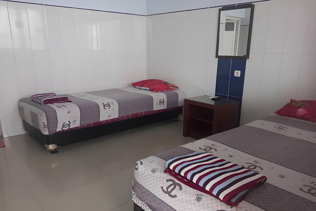 A bedroom with two beds, a nightstand, a mirror, and a red pillow.