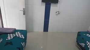 A hotel room with two beds, each with a teal bedspread featuring black and white patterns. There is a television mounted on the wall above the beds, and a blue stripe divider between the beds. - Hotel Orchid Syariah (Tegal)