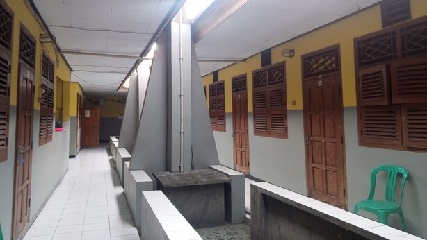 A corridor with tiled flooring, benches, and wooden doors with louvered windows. - Wisma Pelita Syariah Tegal (Tegal)