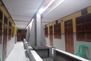 A corridor with tiled flooring, benches, and wooden doors with louvered windows. - Wisma Pelita Syariah Tegal (Tegal)