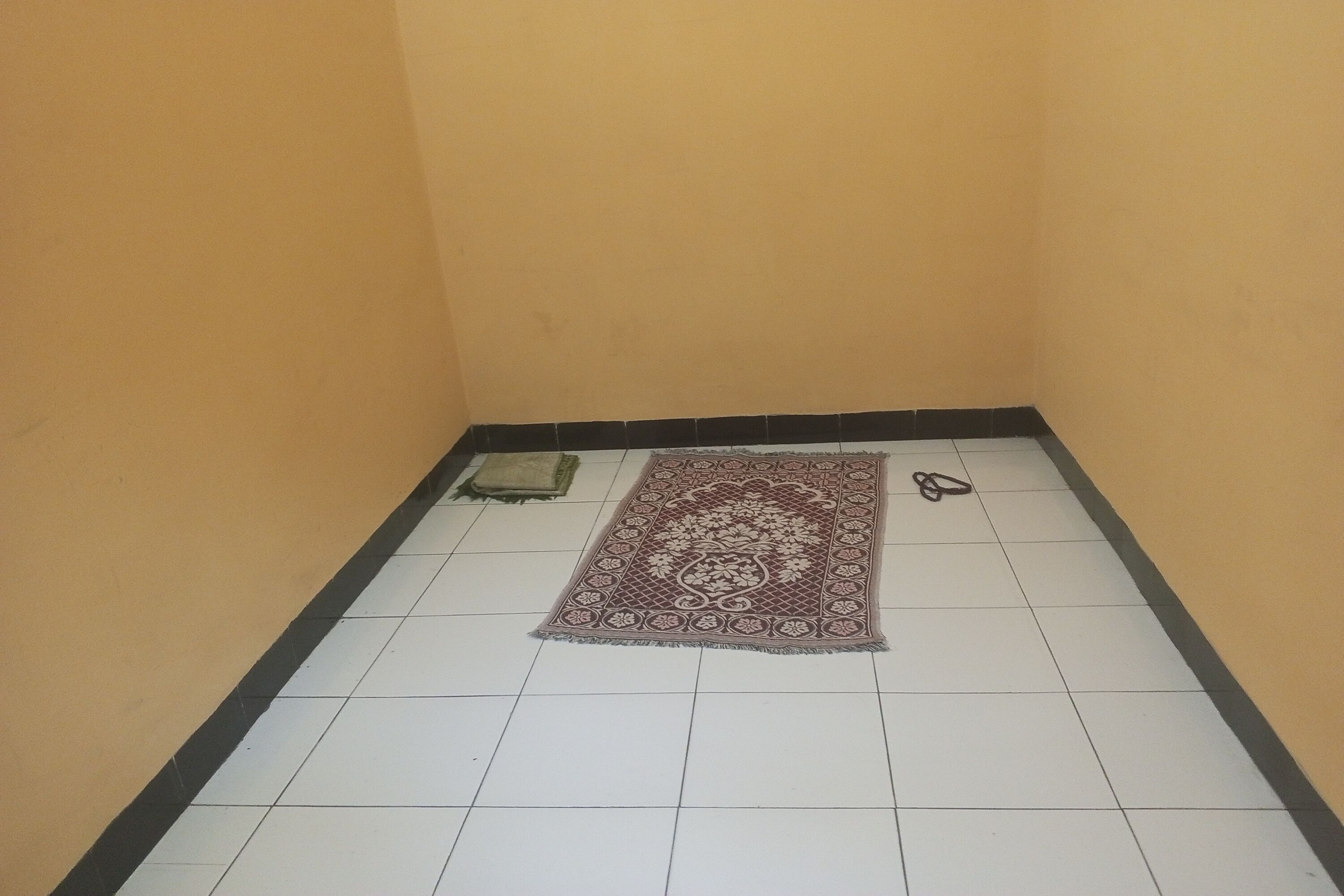 A small, tiled room with a patterned rug and a pair of slippers on the floor.