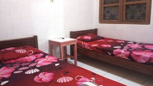 A room with two wooden beds with floral bedding, a small wooden table, and a window with floral curtains. - Wisma Pelita Syariah Tegal (Tegal)