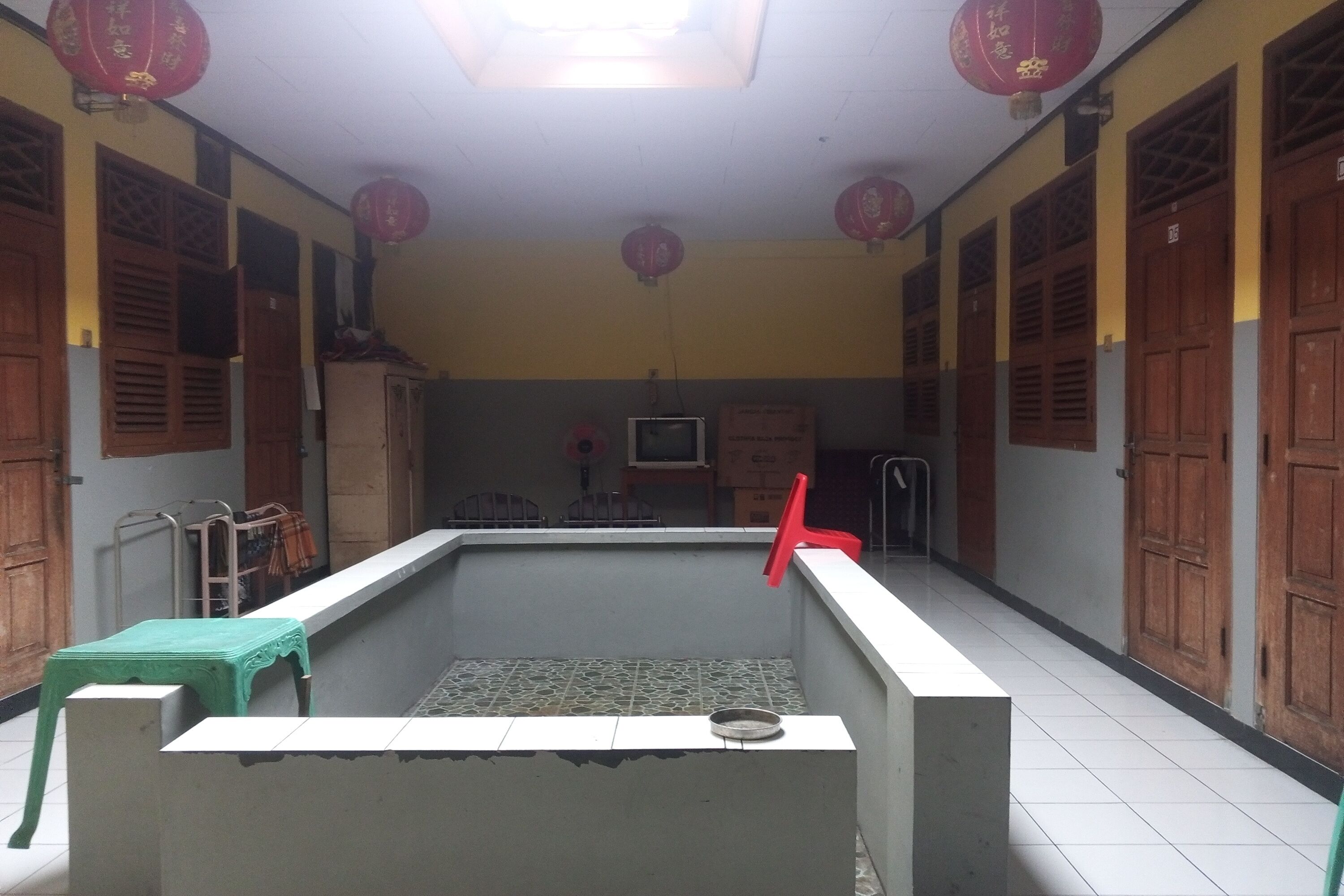 A room with a tiled floor, a green table, a white bench, wooden doors, and red lanterns.