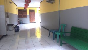A hallway with a green bench, a blue chair, and a wooden door in the background. - Wisma Pelita Syariah Tegal (Tegal)