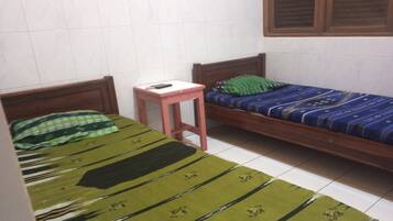 Un alojamiento pequeño, con una sola habitación, cuenta con dos camas de madera, cada una con una colcha estampada diferente. Una pequeña mesa rosa está ubicada entre las camas.