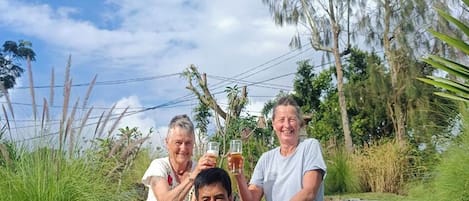 Un grupo de personas sentadas sobre escalones de piedra al aire libre, con un cielo despejado y vegetación de fondo.