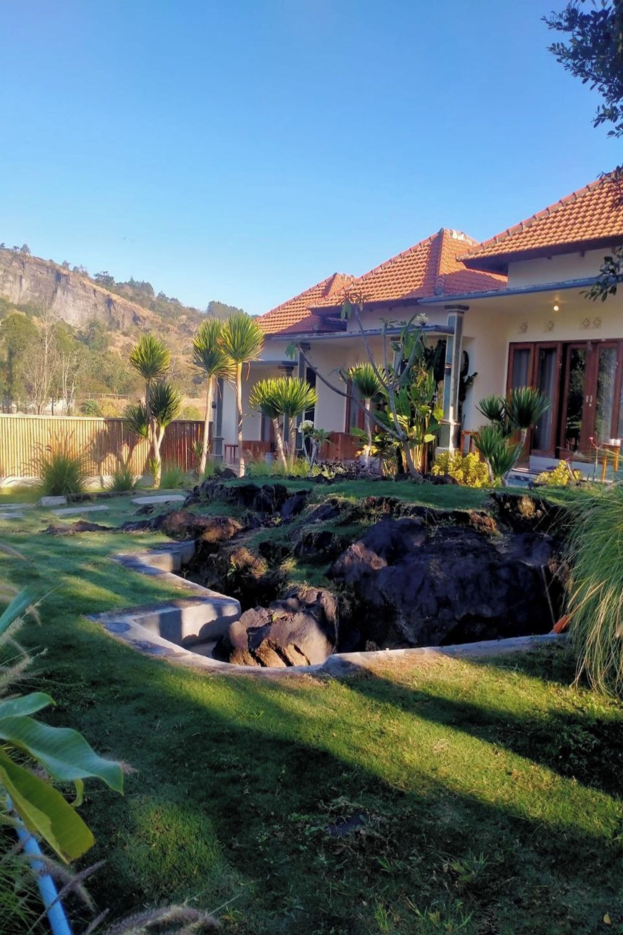 A house with a red-tiled roof, a well-maintained garden with various plants, and a stone retaining wall.