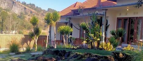 A house with a red-tiled roof, a well-maintained garden with various plants, and a stone retaining wall.