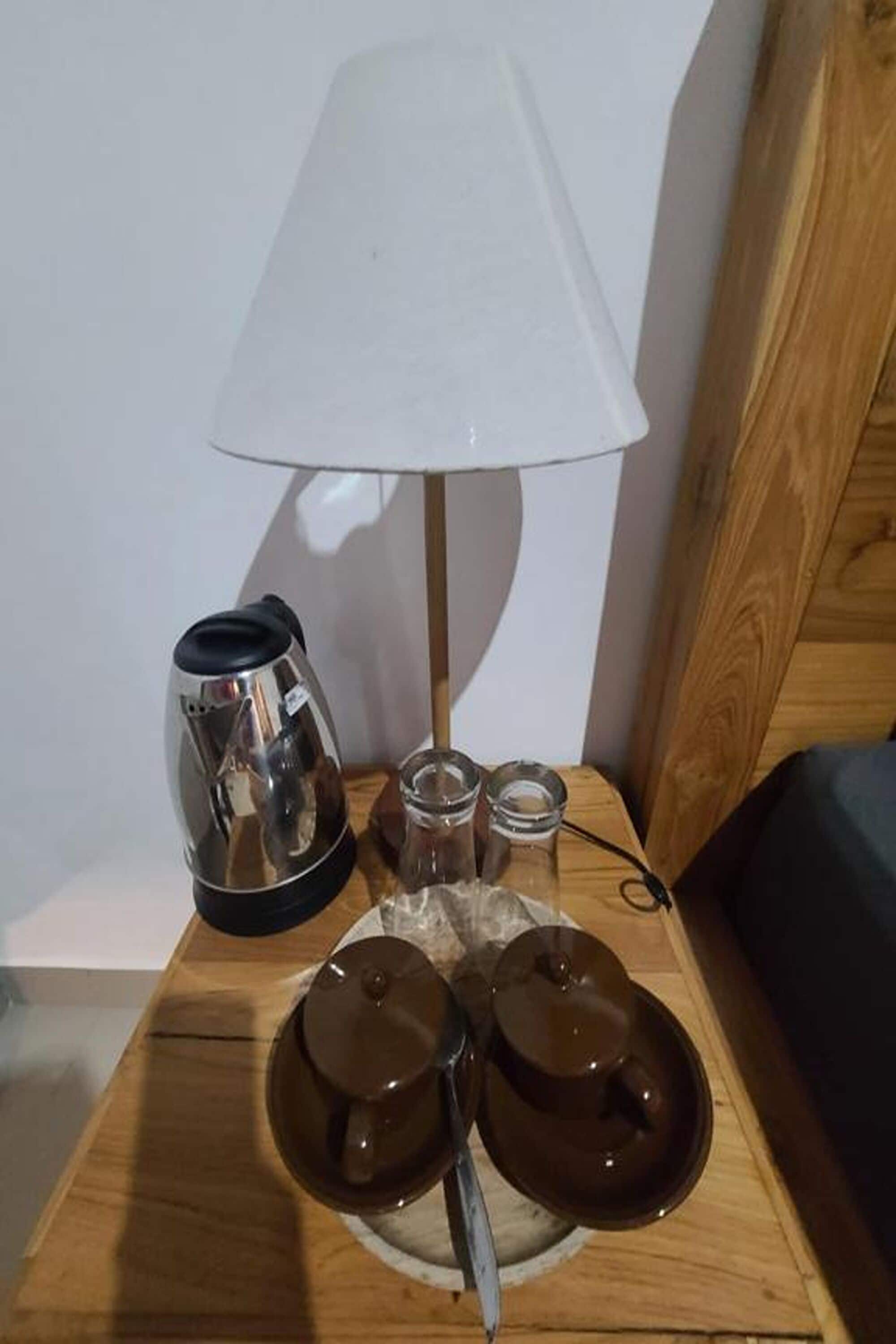 A wooden nightstand with a coffee maker, a lamp, and two teapots on a table.