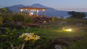 Un belvédère offrant une vue sur une montagne, entouré d’une végétation luxuriante et d’un jardin bien entretenu.