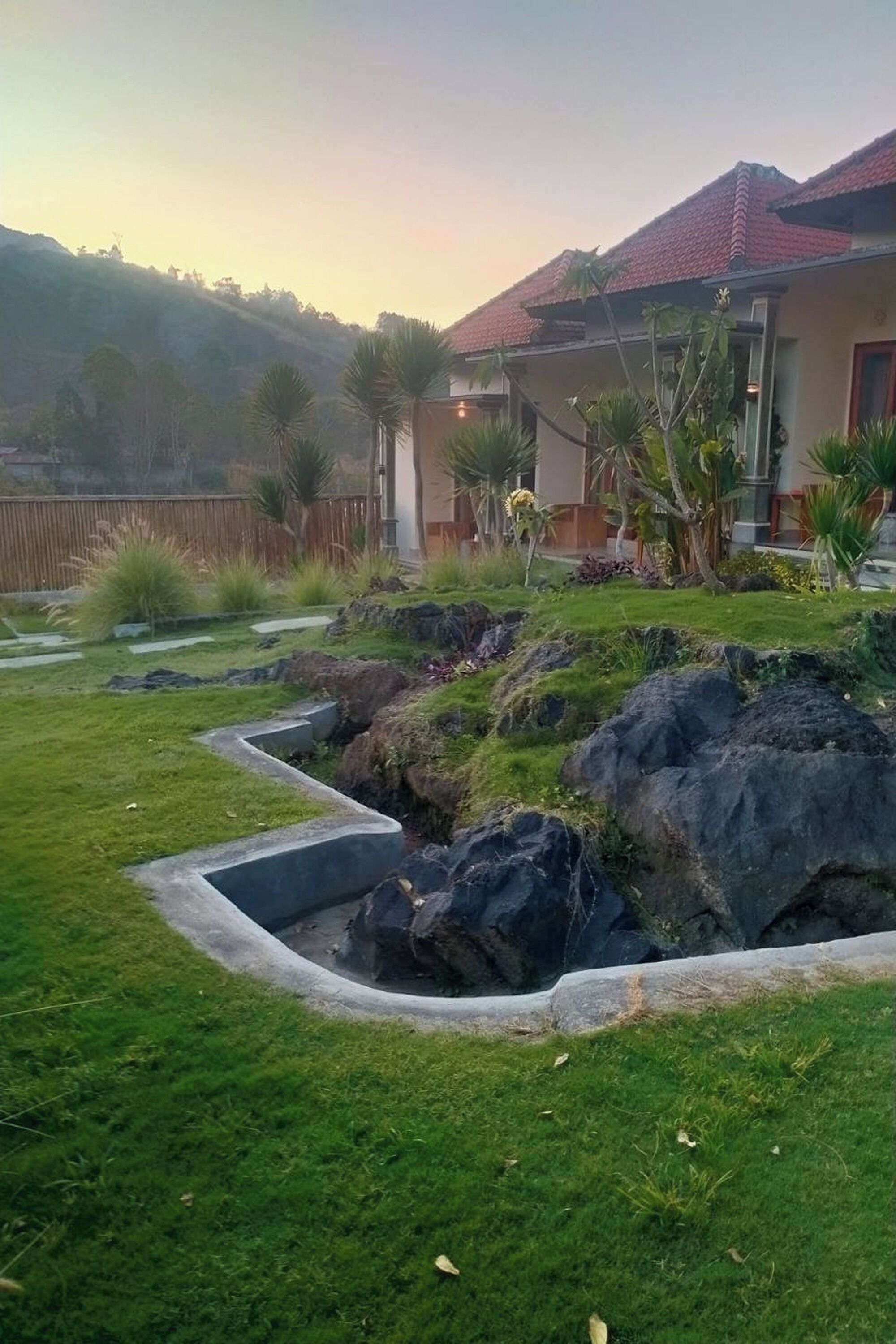 Un barrio residencial con una casa que tiene techo de tejas rojas, césped cuidado y jardín de rocas.