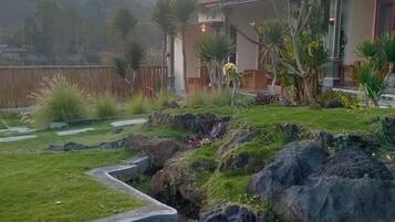 Un barrio residencial con una casa que tiene techo de tejas rojas, césped cuidado y jardín de rocas.
