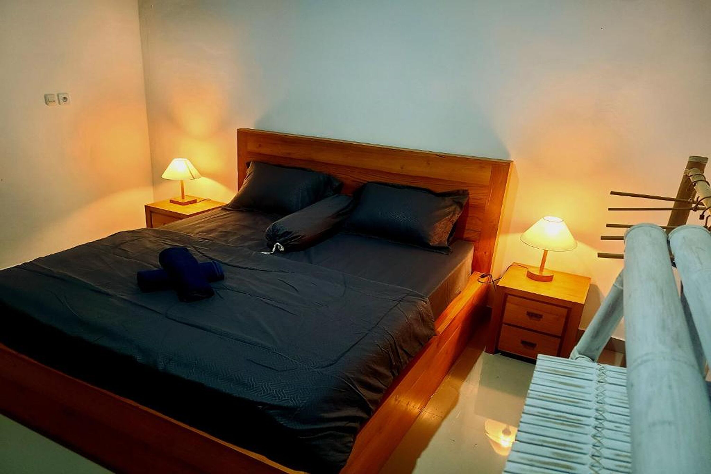 A neatly made bed with a wooden headboard, two bedside tables with lamps, and a visible power outlet on the wall.