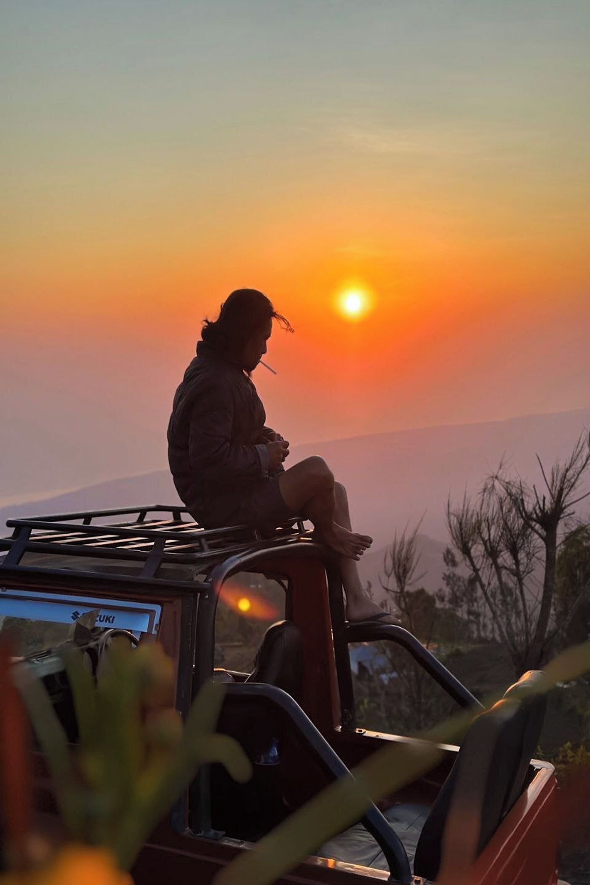 Una persona sentada sobre el techo de un vehículo al atardecer.