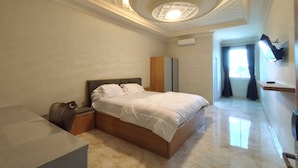 A modern bedroom with a large bed, a wooden nightstand, a suitcase, and a ceiling light fixture. - Maulidia Hotel Syariah & Convention Center (Jambi)
