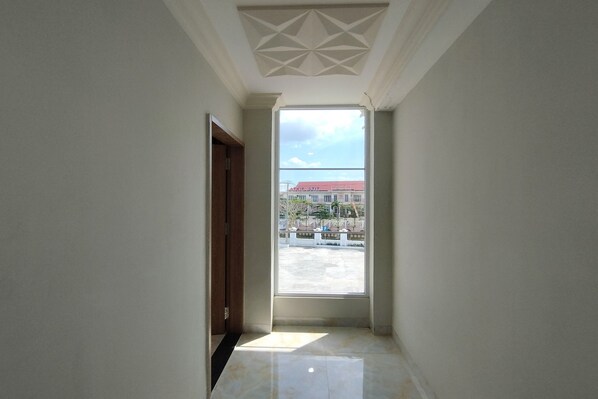 A hallway with a large window, a door, and a ceiling with a geometric pattern.