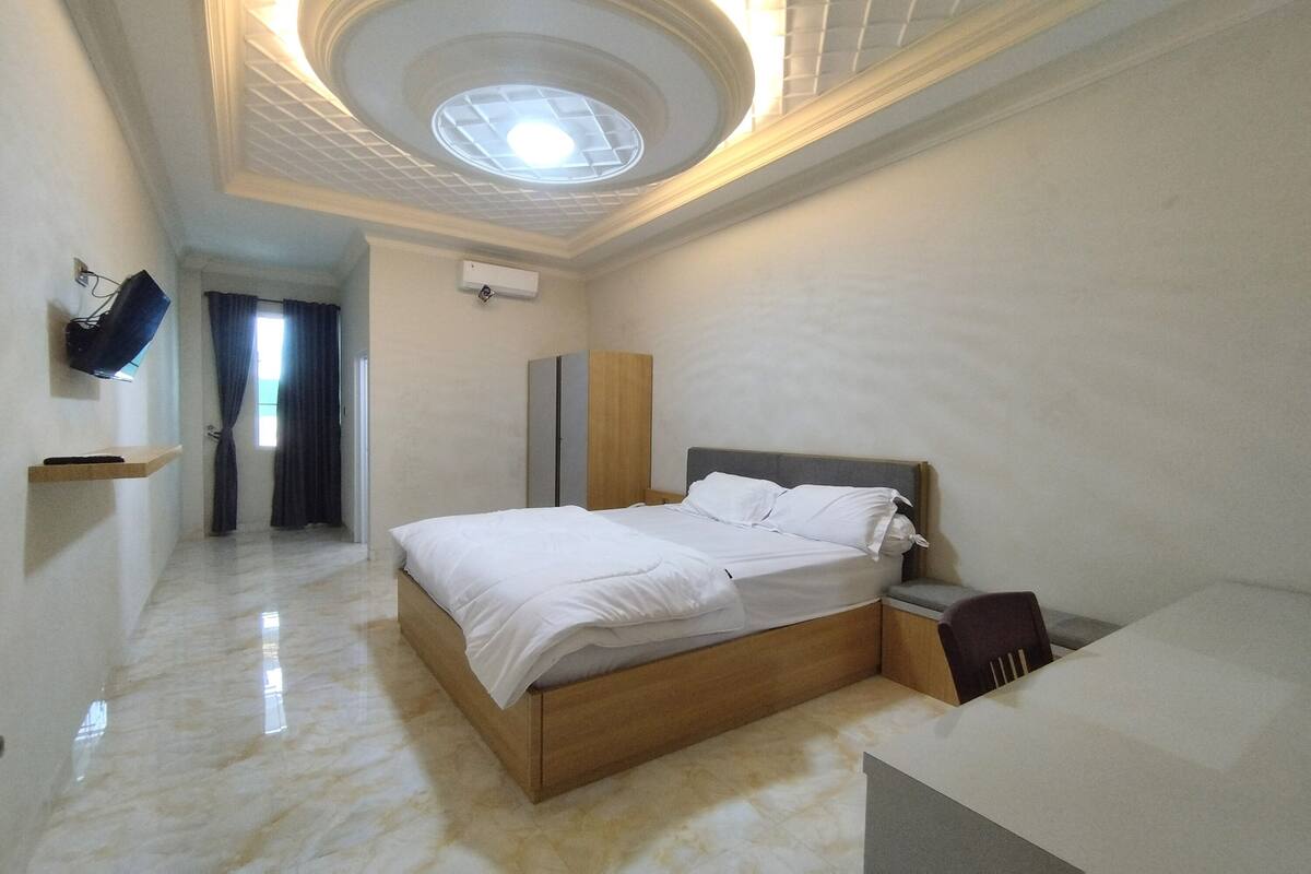 A bedroom with a bed, a bedside table, a chair, a wardrobe, a ceiling light, and a window with curtains.