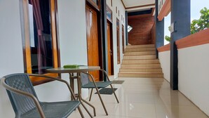 A corridor with a staircase leading to an upper floor, a table with two chairs, and a window with curtains. - Penginapan Bromo Lovero (Sukapura)