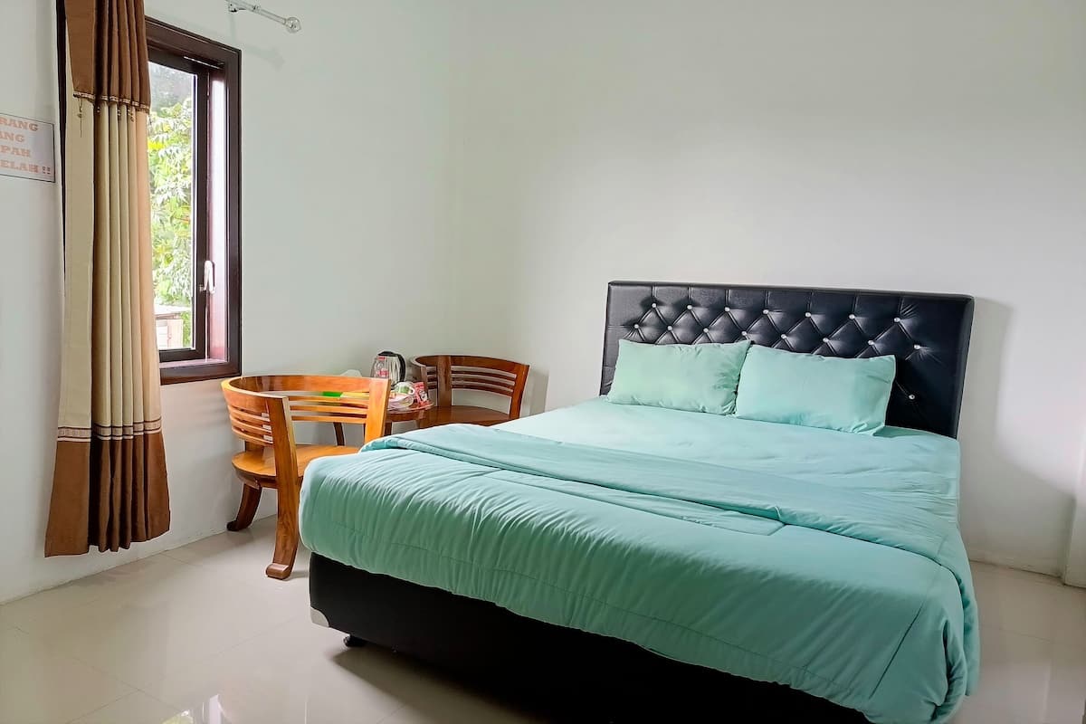 Une chambre à coucher avec un lit, une chaise en bois, une table et une fenêtre avec des rideaux.