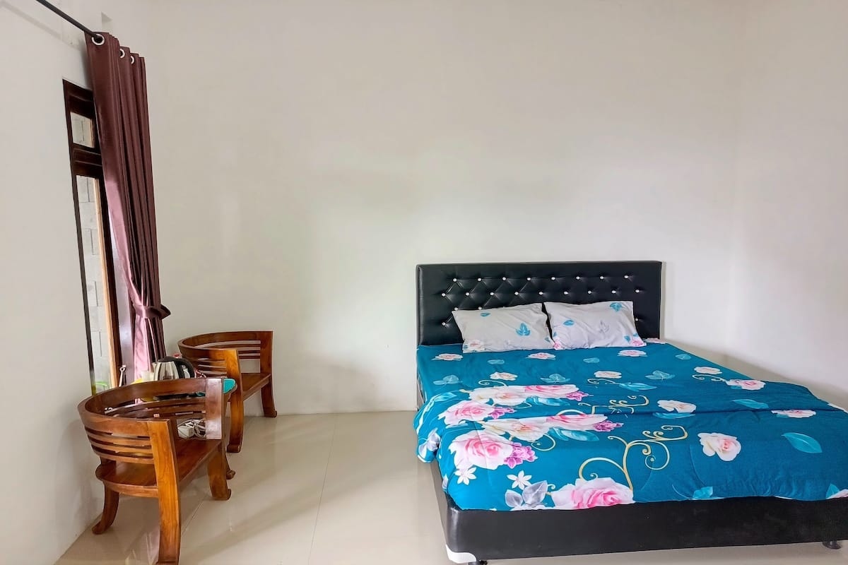 Une chambre à coucher avec un lit, une chaise, un banc en bois et une fenêtre avec des rideaux.