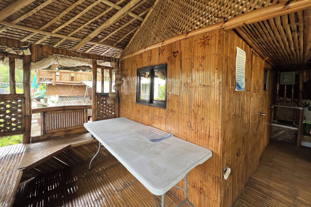 A wooden cabin with a table and benches, a window, and a wooden deck.