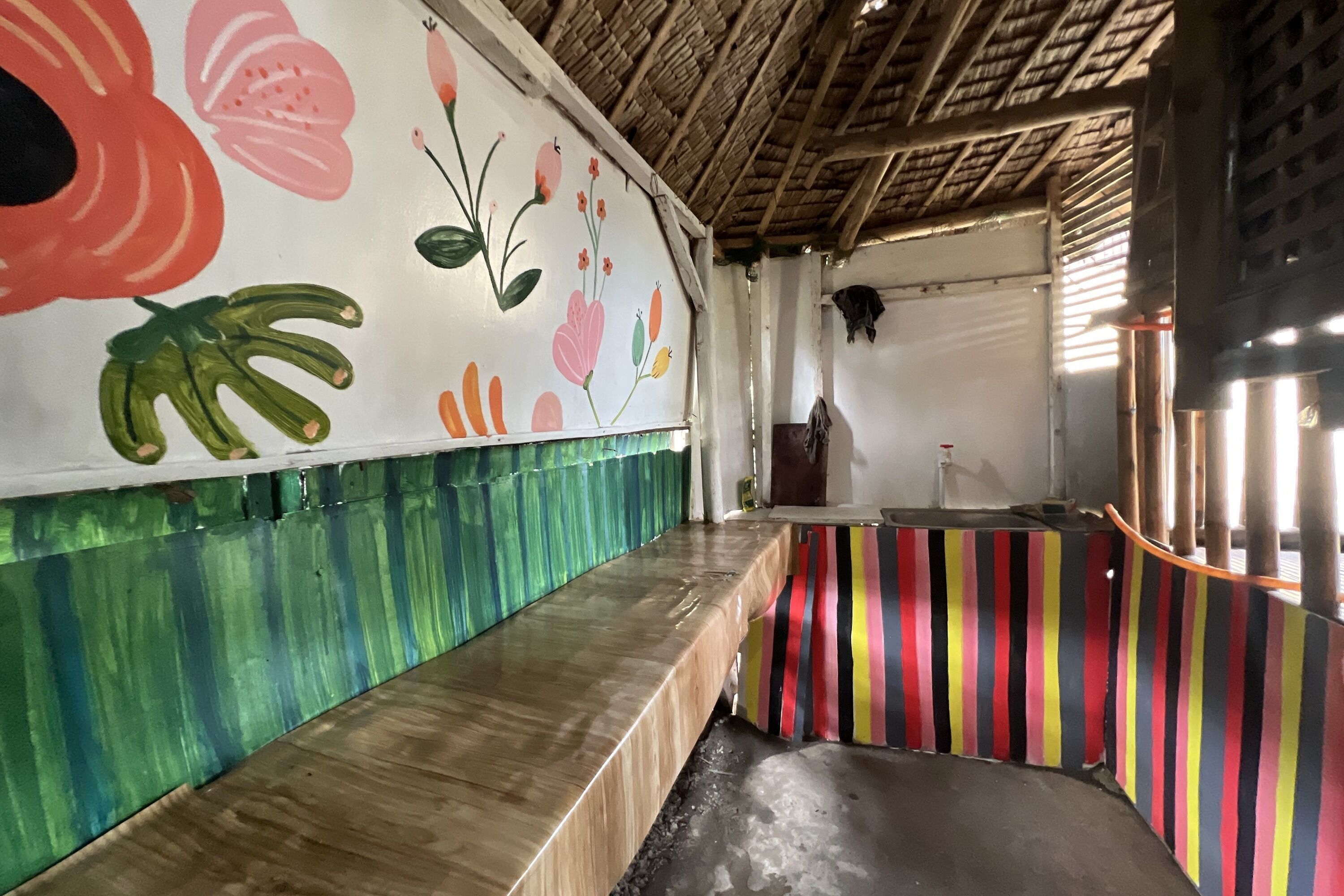 A room with a wooden bench, a colorful striped counter, and a wall with floral artwork.