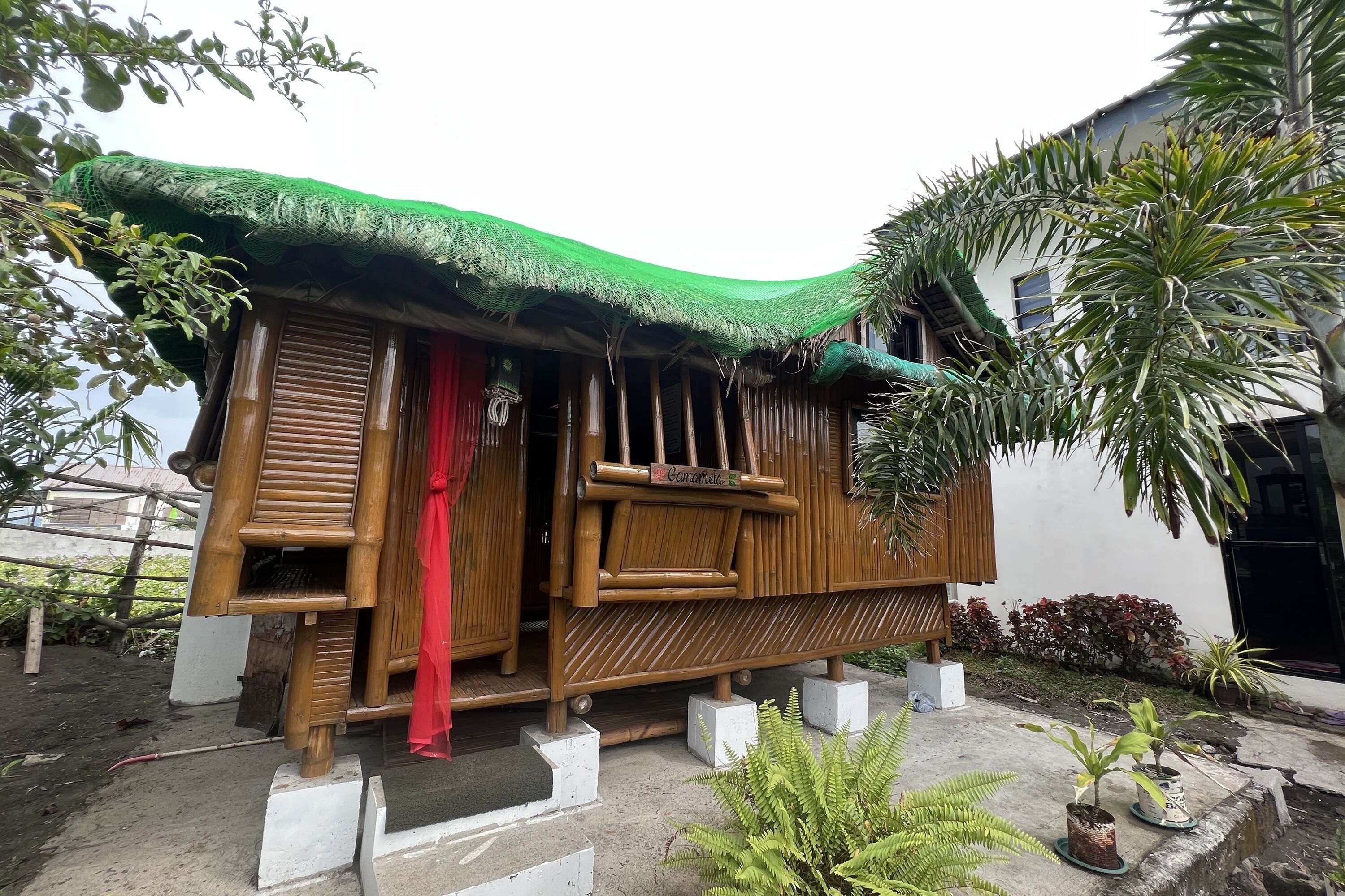 A traditional bamboo house with a thatched roof, a wooden door, and a small porch area.