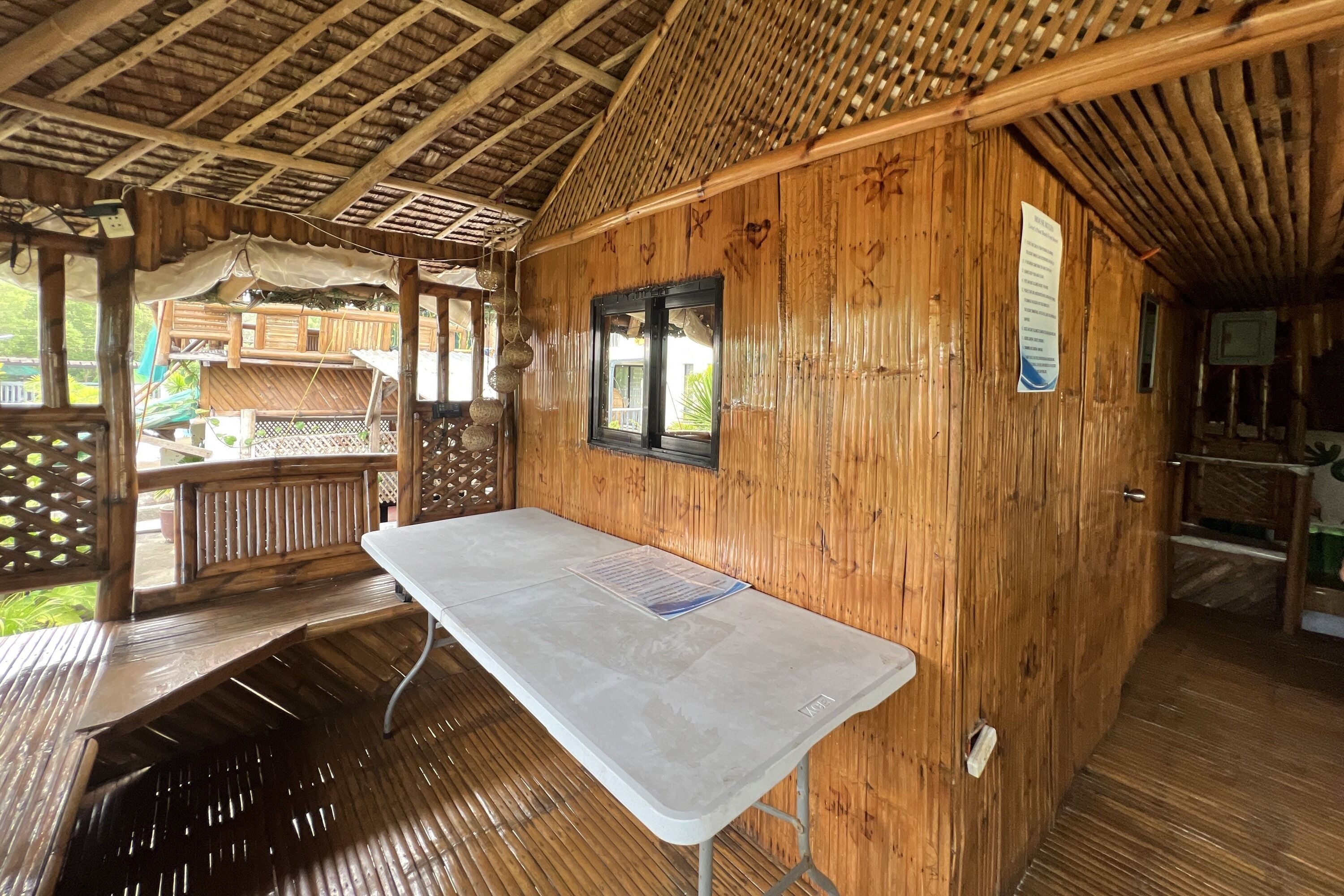 A wooden cabin with a table and benches, a window, and a wooden deck.