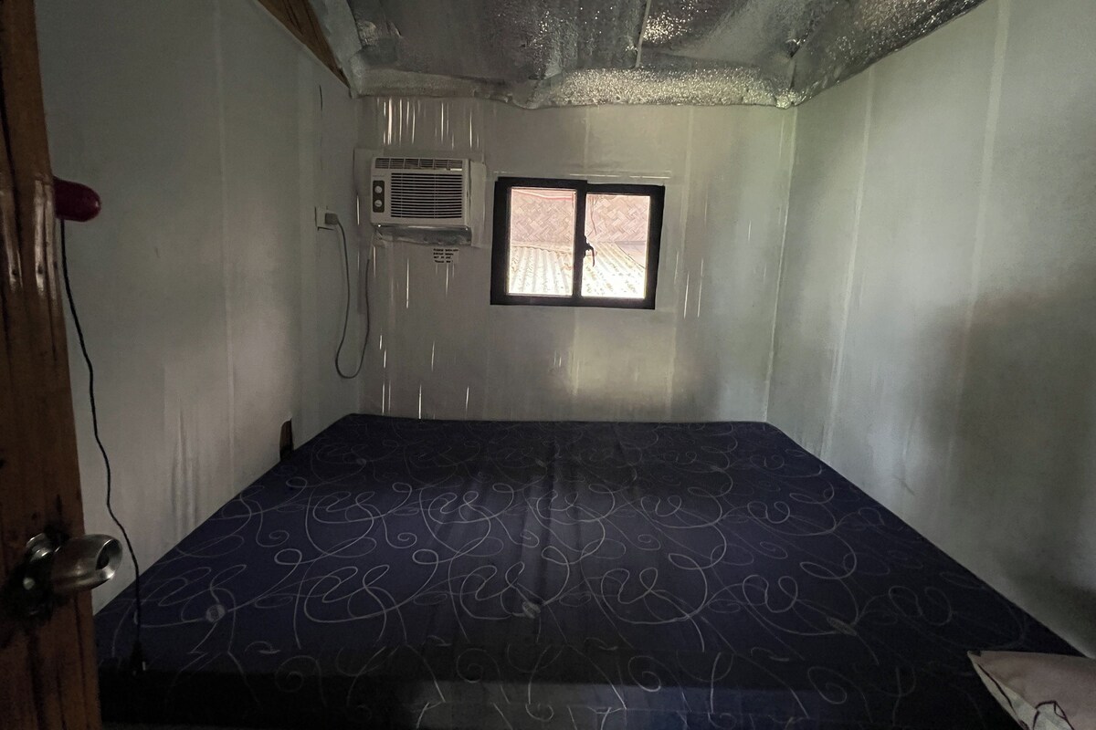 A small room with a bed, an air conditioning unit, and a window.
