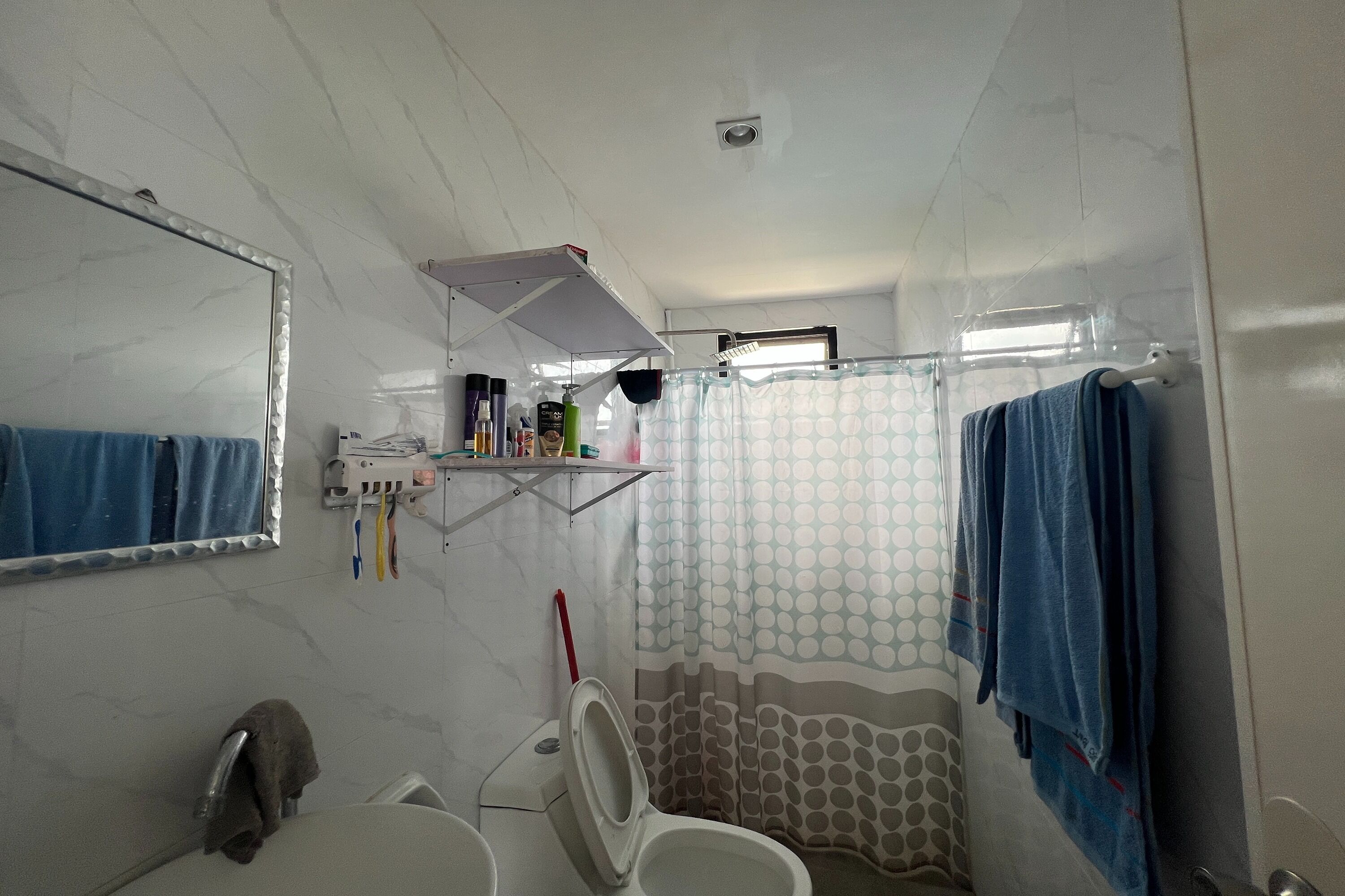 A bathroom with a toilet, sink, mirror, shower curtain, and a towel rack.