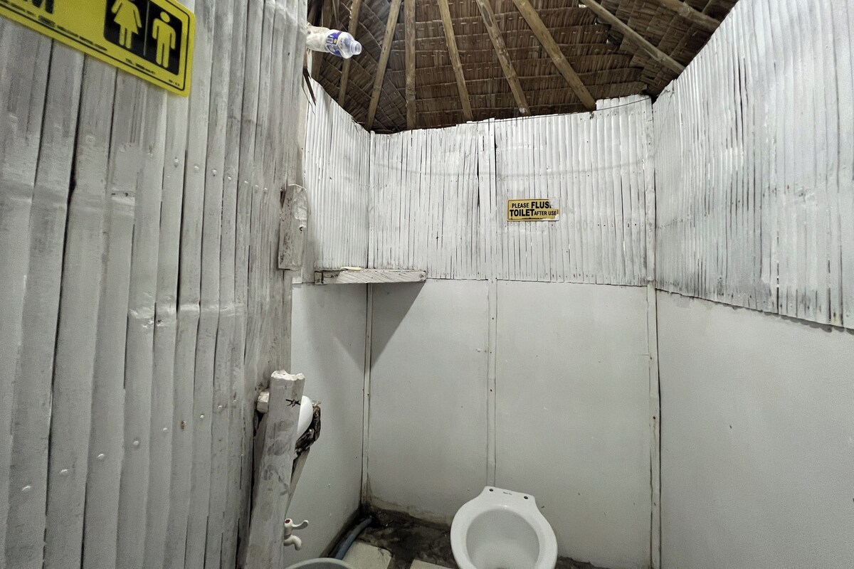 A small, enclosed bathroom with a single toilet, a sign indicating the use of the toilet, and a sign warning to flush after use.