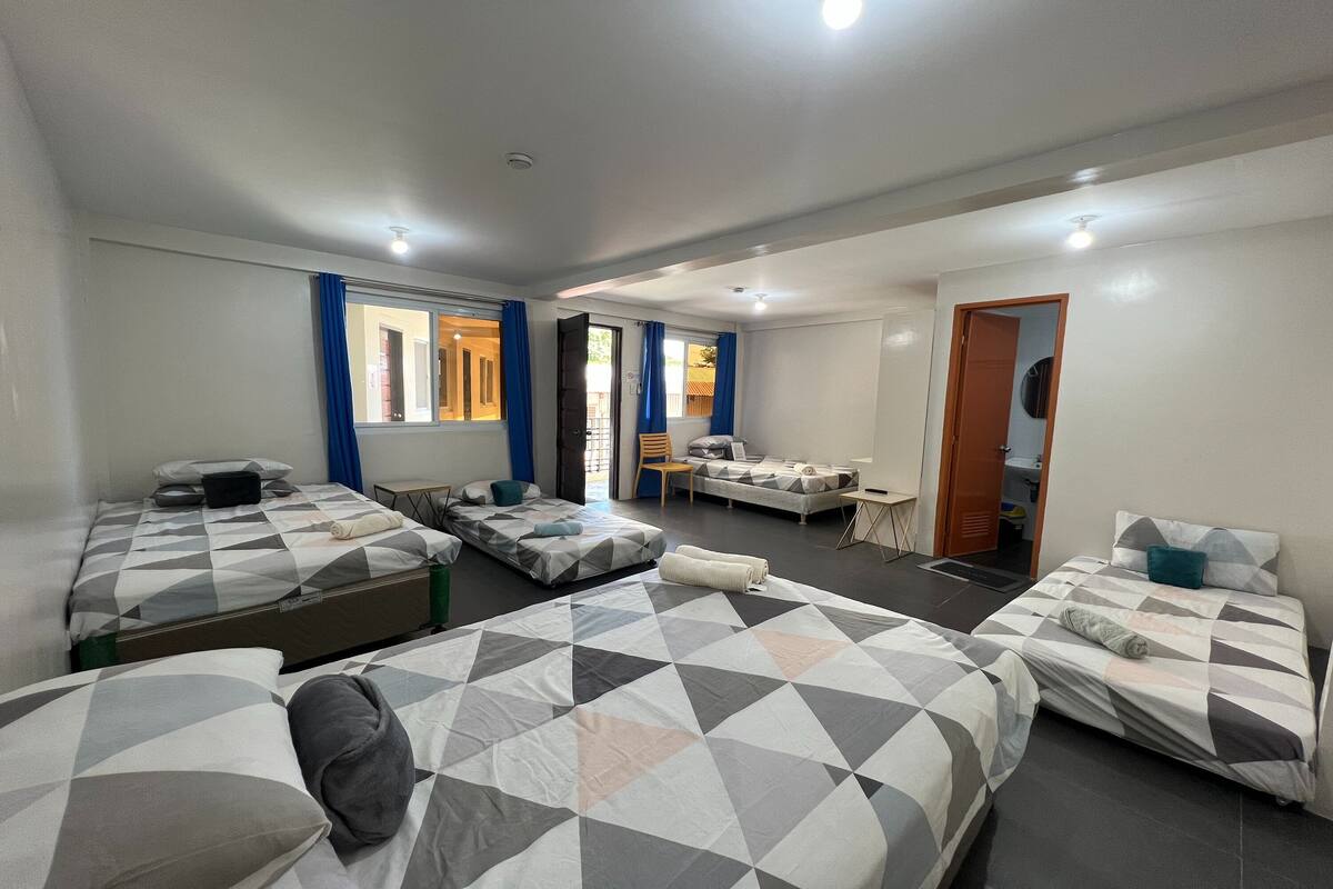 A hotel room with four beds, a small table, and a chair.