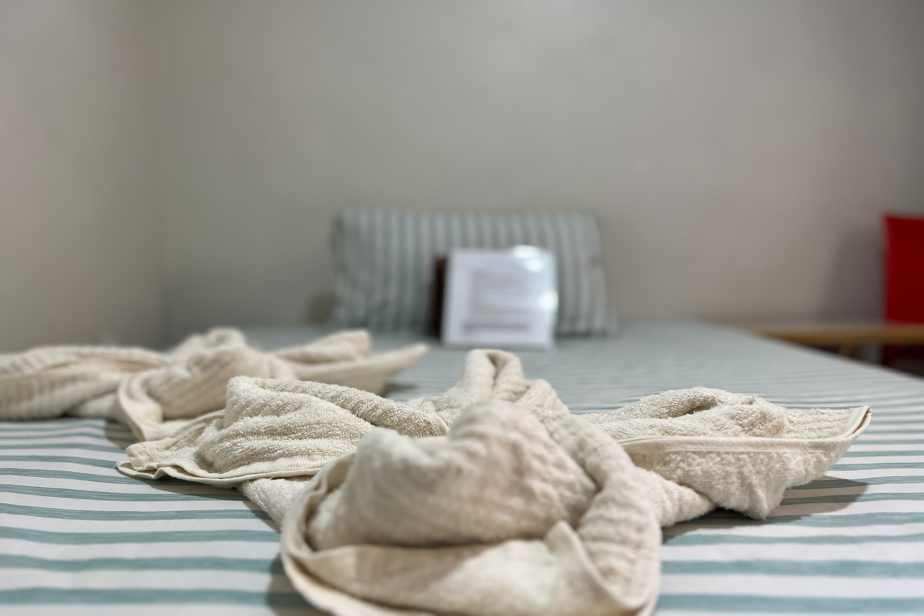 A bed with a striped bedspread and several folded towels on it.